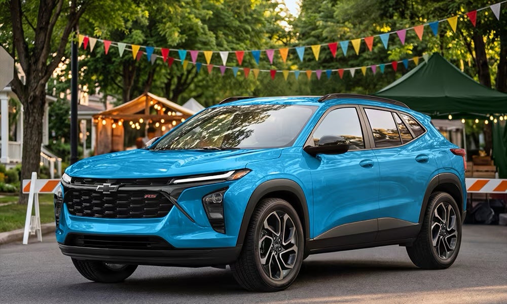 A bright blue 2026 Chevrolet Trax SUV parked in front of a block party