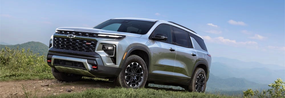 A silver 2027 Chevrolet Traverse SUV driving up a high dirt road