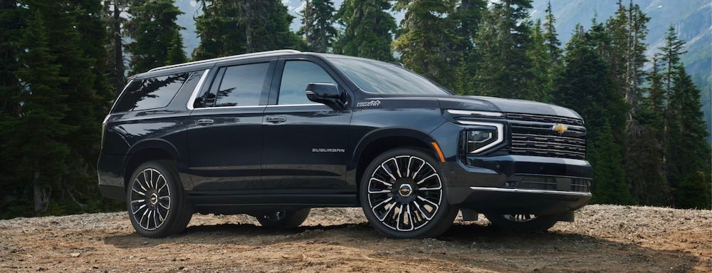 A black 2027 Chevrolet Suburban SUV with pine trees in the background